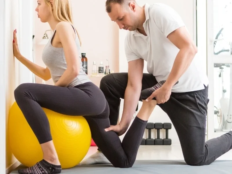 A physical therapist assisting a patient with a stability-ball stretch