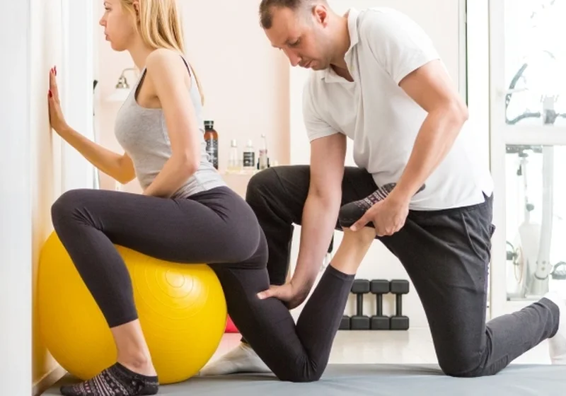 A physical therapist assisting a patient with a stability-ball stretch